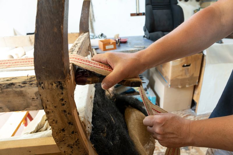 Upholsterer tightening a new strap on an old armchair, traditional craft skill to preserve antique furniture, copy space, selected focus, narrow depth of field