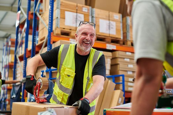 Warehouse worker packing boxes and smiling.