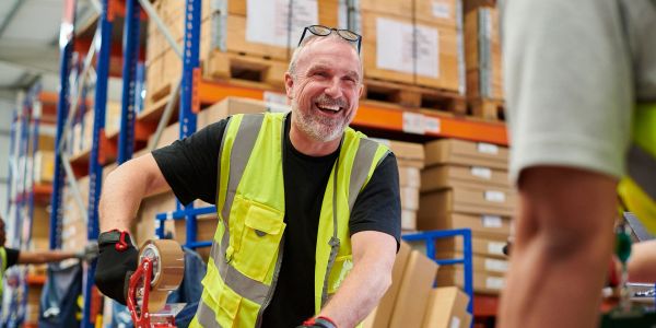Smiling warehouse worker in a safety vest organizing packages.