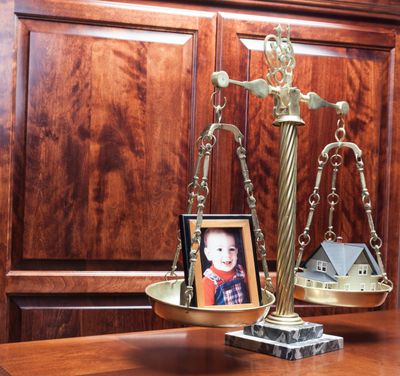 A balance scale weighing a baby photo against a model house.