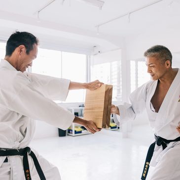 Two martial artists preparing to break a wooden board indoors.
