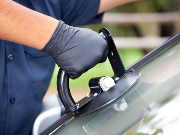 Close-up of a worker using a suction cup tool on a car windshield.