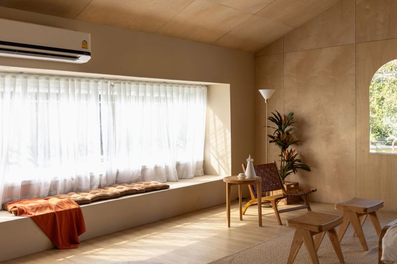 A harmonious blend of modern design meets natural aesthetics. Sunlight streams through white curtains, casting a gentle glow on wood textures and earth-toned furnishings, creating an inviting space