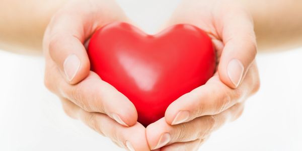 Hands gently holding a red heart symbol.