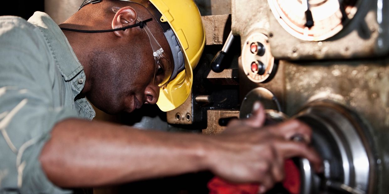 Worker operating industrial machinery wearing safety gear.