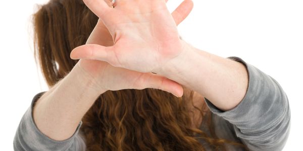 Person covering face with hands, hiding behind long curly hair.