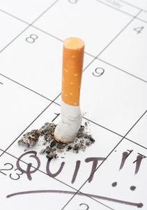 A cigarette butt extinguished on a calendar with "QUIT!!" written.