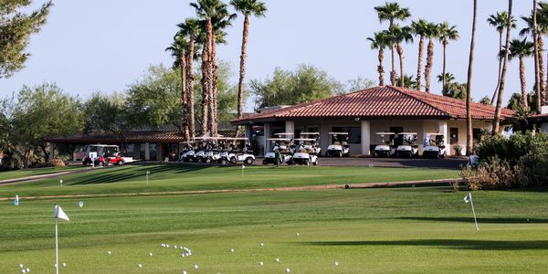Golf carts lined up near a clubhouse on a sunny golf course.
