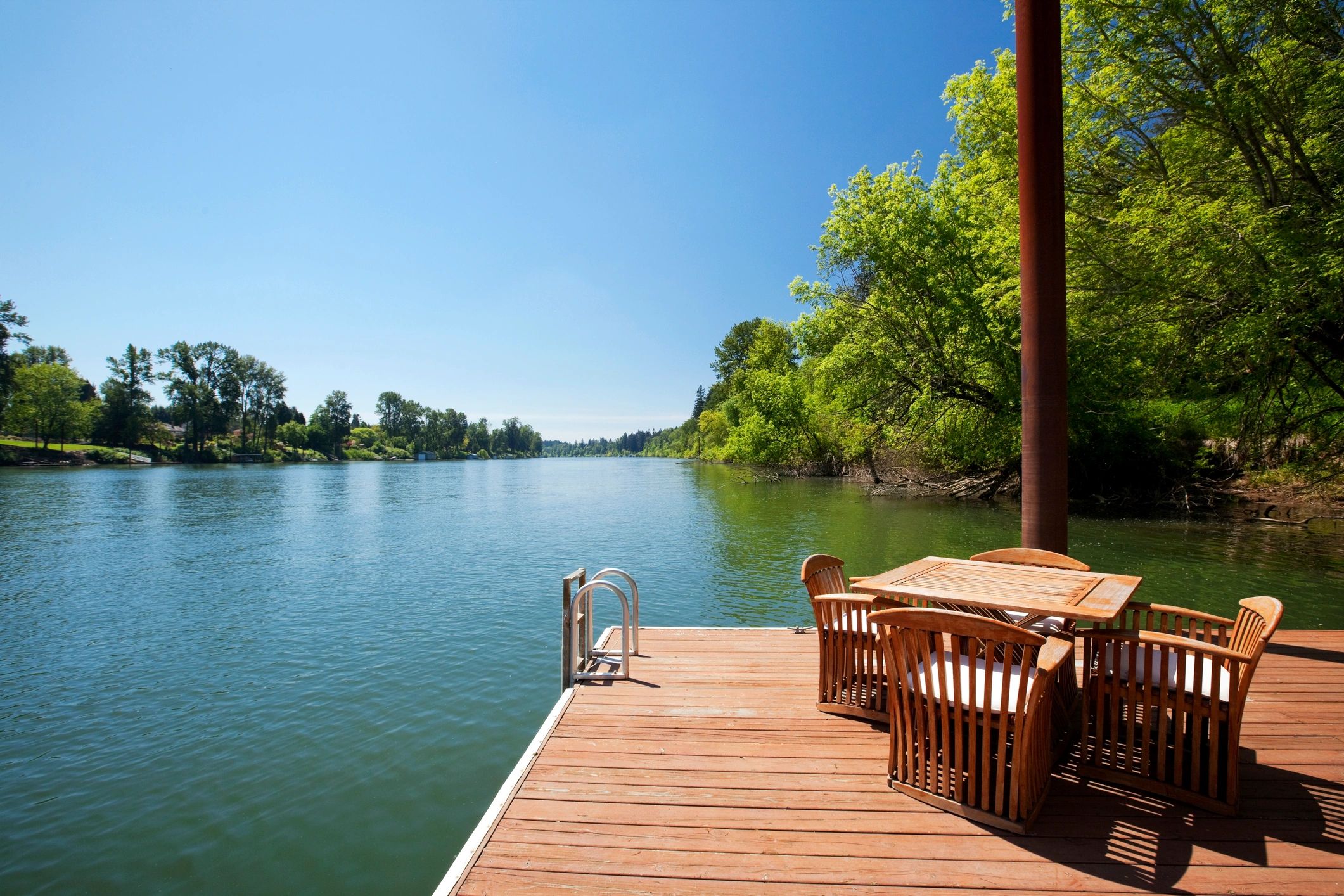 Wooden dock with chairs overlooking a calm river on a sunny day.