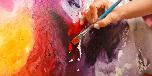 A hand painting vibrant red on a colorful abstract canvas.