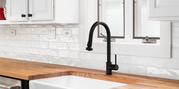Modern kitchen sink with black faucet and wooden countertop.