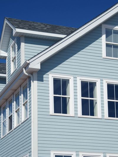 Close-up of a blue house exterior with white window frames against a clear sky.