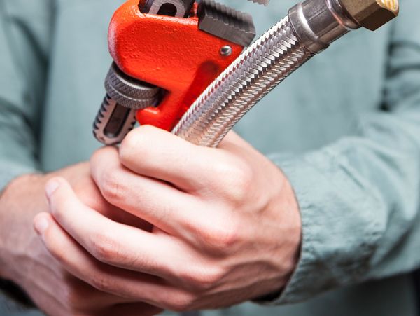 A person holding a red pipe wrench and a flexible metal hose.