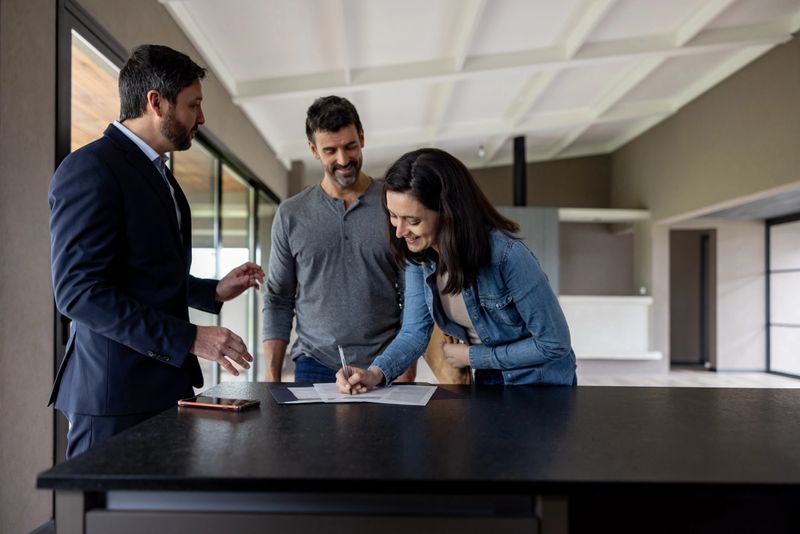 Happy Latin American couple buying a house and signing the deed in front of their real estate agent - home ownership concepts