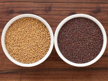 Two bowls filled with yellow and black mustard seeds on a wooden table.