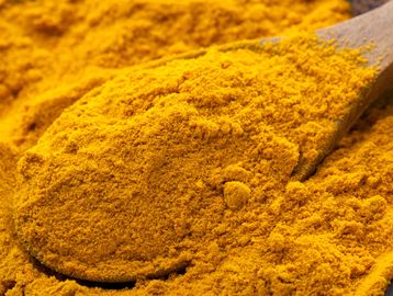 Close-up of ground turmeric powder with a wooden spoon.