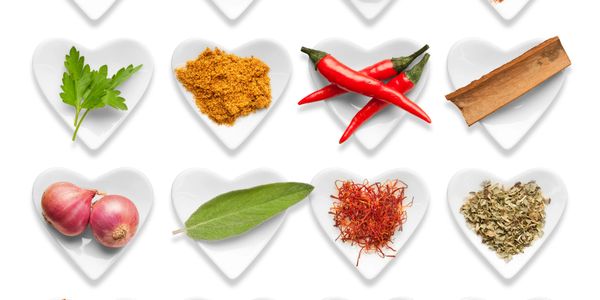 Various spices and herbs arranged in heart-shaped dishes on a white background.