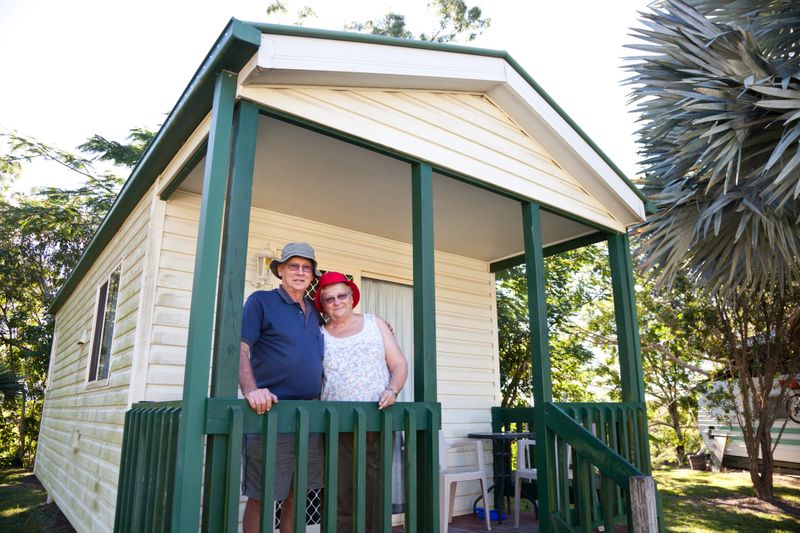 Happy retired senior couple standing in front of a holiday cabin aa affectionately with arms around each other.