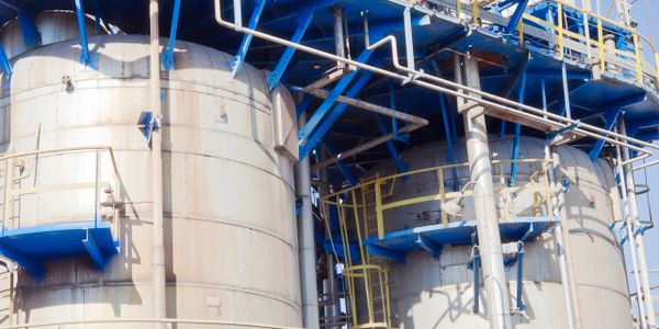 Industrial storage tanks with blue metal framework and piping under clear sky.