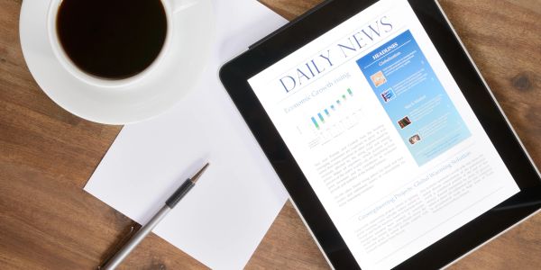 Tablet displaying news beside coffee, pen, and paper.