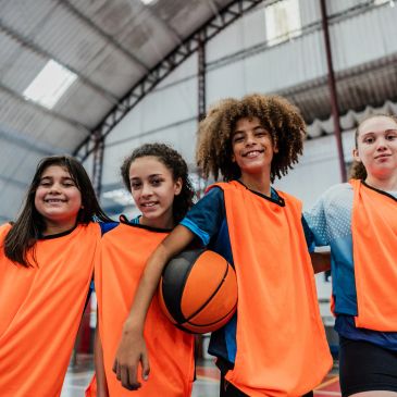 Four smiling kids in orange sports jerseys with a basketball.