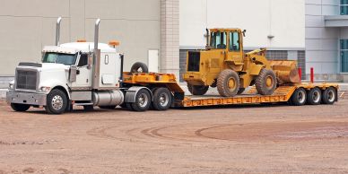 A truck transporting a yellow bulldozer on a flatbed trailer.
