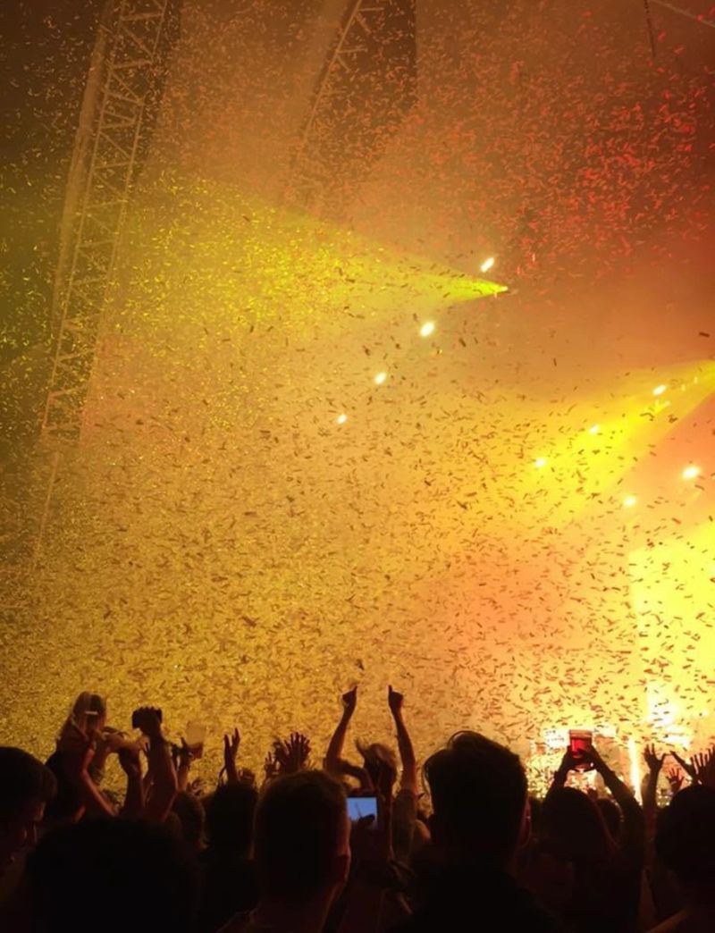 Imagine the electric atmosphere of a Chase and Status music gig, where silhouettes of people create a pulsating crowd against a backdrop of vibrant orange and yellow lights. The stage is alive with energy, and hands are raised in the air in unison, reaching for the rhythm that reverberates through the venue.

The concert is a sensory feast, with the beats of Chase and Status echoing through the air, creating an immersive experience for the enthusiastic crowd. The orange and yellow lights dance in harmony with the music, casting dynamic shadows and illuminating the faces of those caught in the rhythm.

Confetti rains down, adding a touch of celebration to the scene. It's a moment of collective joy, where the crowd is immersed in the music, lost in the magic of the performance. Drinks are raised in toasts, and the air is filled with the sounds of laughter and cheers.

The atmosphere is infectious, filled with the exuberance of a shared musical journey. Each beat connects the audience, creating a sense of unity and camaraderie. It's a snapshot of pure happiness, a memory etched in the minds of those lucky enough to be part of this unforgettable concert experience.