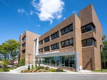 Modern brick College of Business building with large windows under a blue sky.