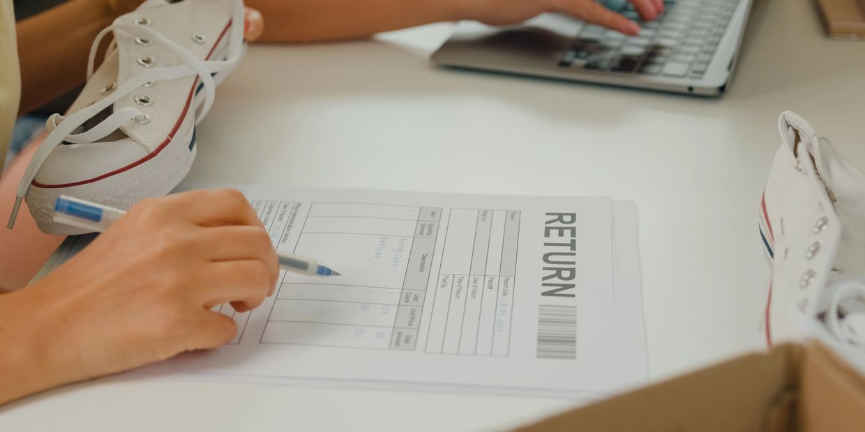Person filling out a shoe return form while holding a white sneaker.
