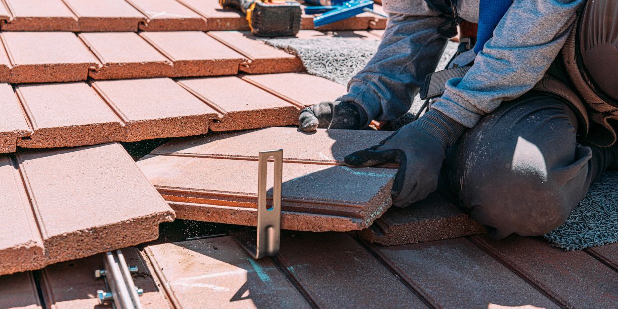 Worker installs roofing tiles with gloves on.