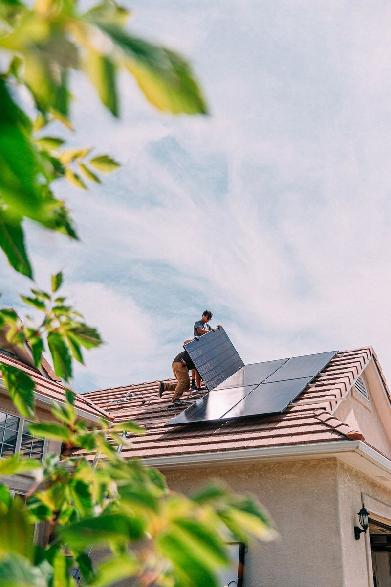 Low Angle view of Two Caucasian Male Homeowners or DIY-ers installing Solar Panels to Brackets on a Suburban Home with Clay Tiles in the Summer