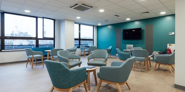 Modern lounge area with teal chairs and large windows providing natural light.