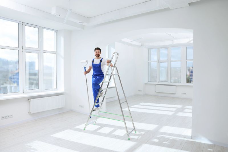 Handyman with roller on step ladder in room. Ceiling painting