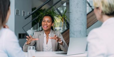 A woman in business attire speaking enthusiastically during a meeting.