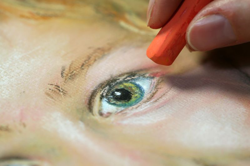Woman painting a portrait of a child with pastel crayons.