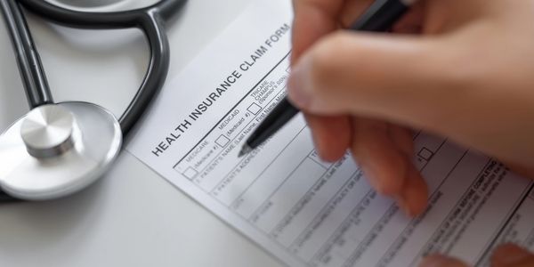 A person filling out a health insurance claim form beside a stethoscope.
