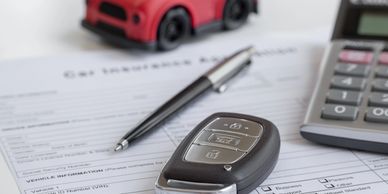 Car key on insurance form with pen and calculator.