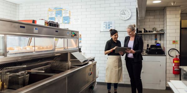 Two women discussing something on a tablet in a commercial kitchen.