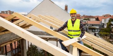 A construction worker in safety gear working on a wooden roof frame.