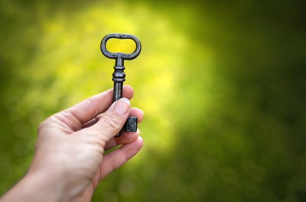 Hand holding an old metal key against a green blurred background.