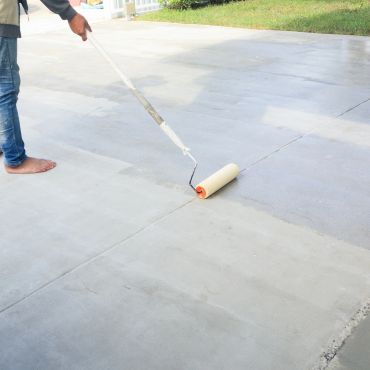 Person applying coating on concrete floor with roller brush.