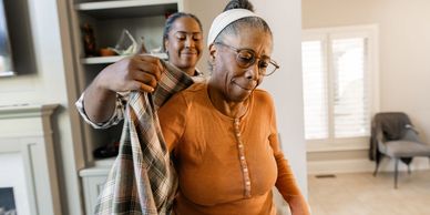A woman helps an elderly woman put on a jacket.