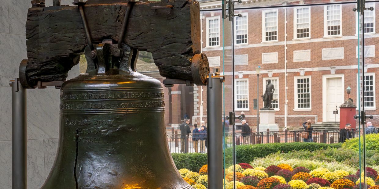The Liberty Bell displayed indoors with a historic building outside.