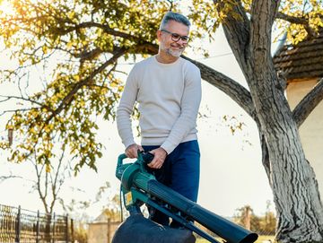 Man using a leaf blower to clear fallen leaves in a yard.