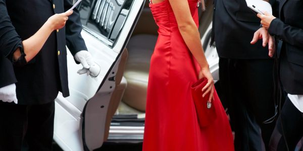 Woman in red gown arrives at event with media and security.