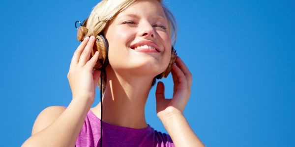 Young woman enjoying music with headphones against a clear blue sky.