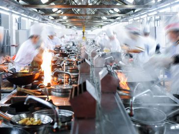 Busy professional kitchen with chefs cooking at multiple stations.