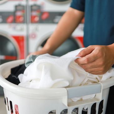 Person folding white laundry in a basket near washing machines.