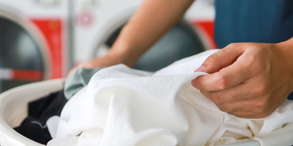 Person handling laundry in a basket at a laundromat.
