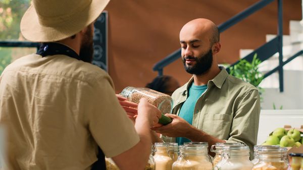 Man buying grains in a bulk store from a vendor wearing a hat.